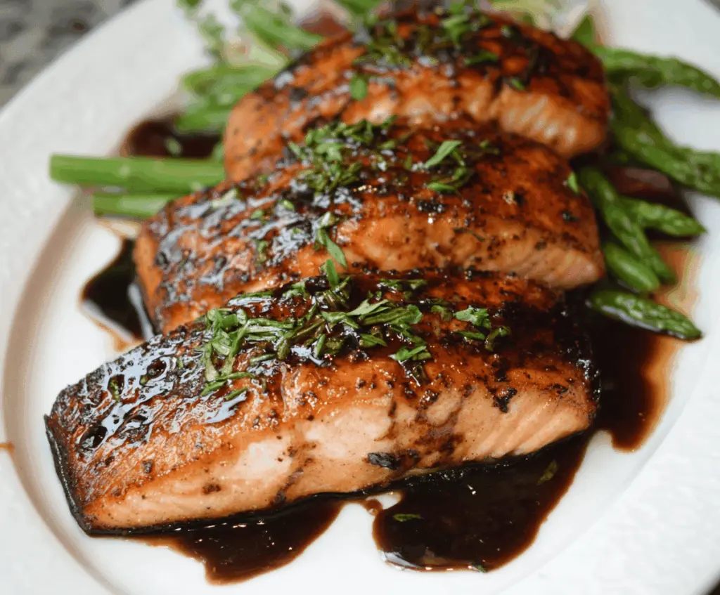 Delicious balsamic glazed salmon fillet garnished with fresh herbs on a white plate, served with colorful vegetables.