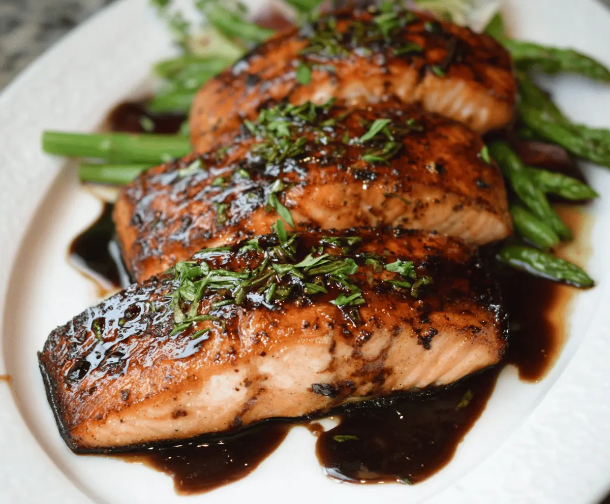 Delicious balsamic glazed salmon fillet garnished with fresh herbs on a white plate, served with colorful vegetables.
