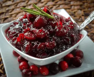 Close-up of homemade brown sugar maple cranberry sauce in a glass bowl with fresh cranberries and maple syrup