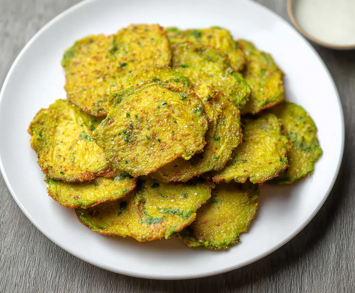 Crispy homemade avocado chips on a white plate, garnished with herbs.