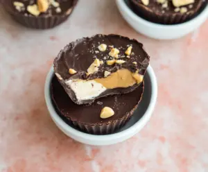Delicious Greek Yogurt Peanut Butter Cups on a white plate with melted chocolate and crunchy peanuts