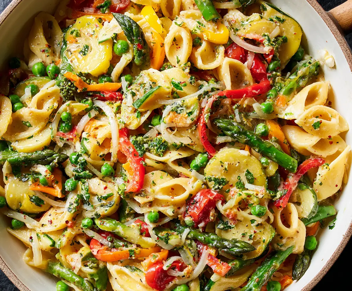 Colorful Pasta Primavera with fresh vegetables and herbs served on a white plate.