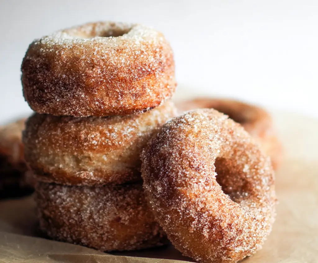 Freshly made sourdough apple cider donuts dusted with powdered sugar on a rustic plate.