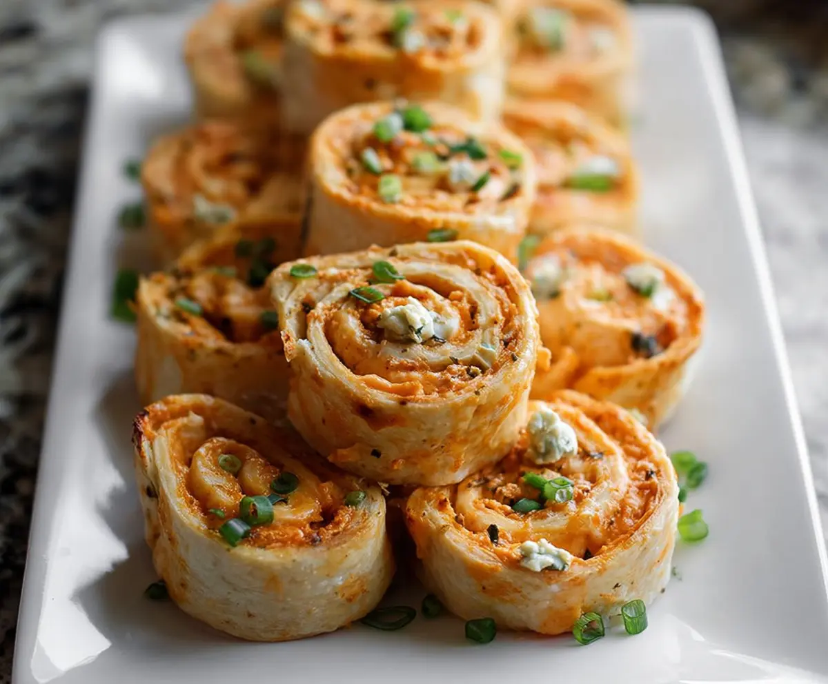 Delicious buffalo chicken pinwheels garnished with green onions on a white plate.