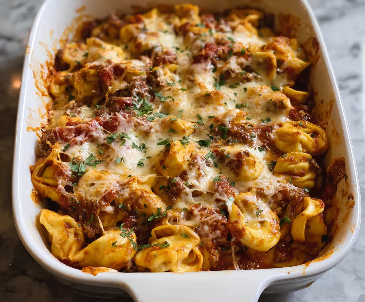 Creamy Million Dollar Tortellini Casserole topped with melted cheese and herbs in a baking dish.