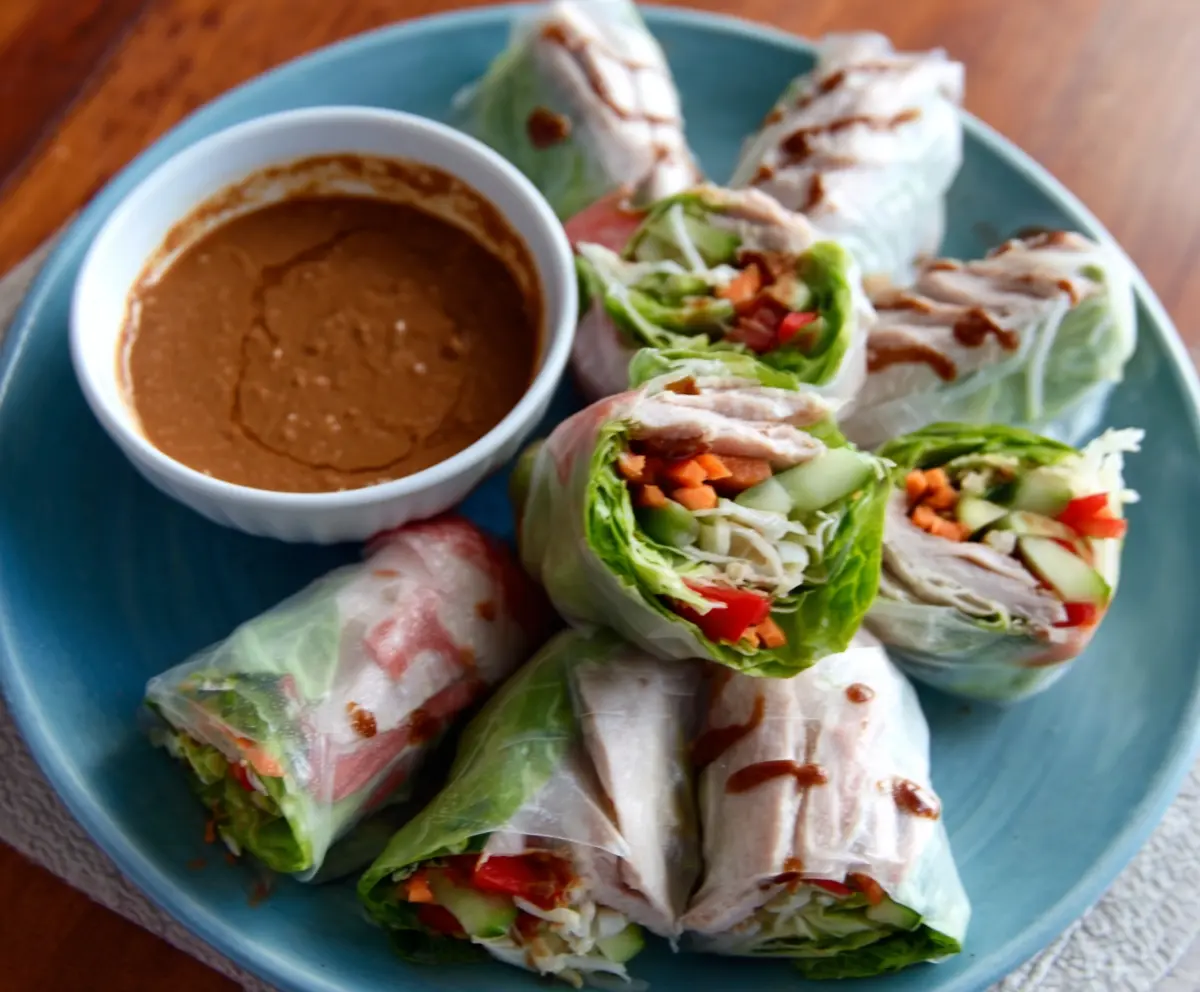 Crispy pork spring rolls served with a zesty peanut lime dipping sauce on a white plate.